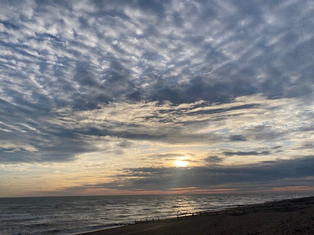 Beautiful sunset over the South Coast. Lots of broken cloud with light behind it. Yellow sun setting behind a cloud and sky turning orange just above the sea.