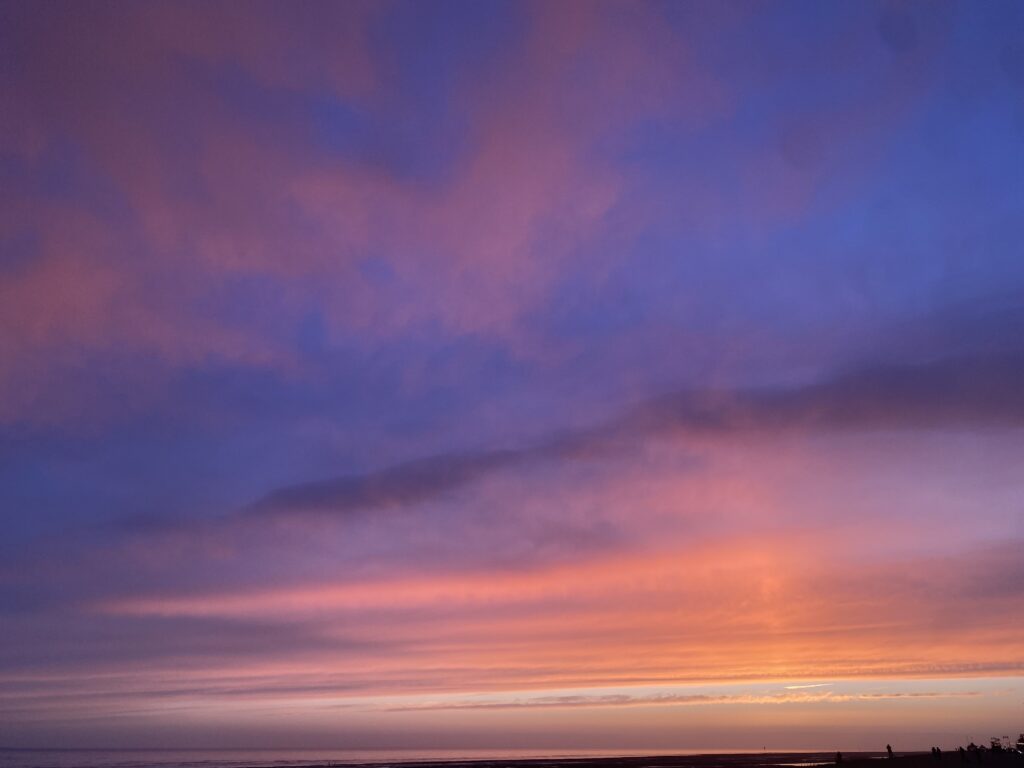 Beautiful and colourful sunset over the South Coast, UK. Sky is blue, purple, orange with pinky clouds. Embodiment practice takes in the surrounding beauty.