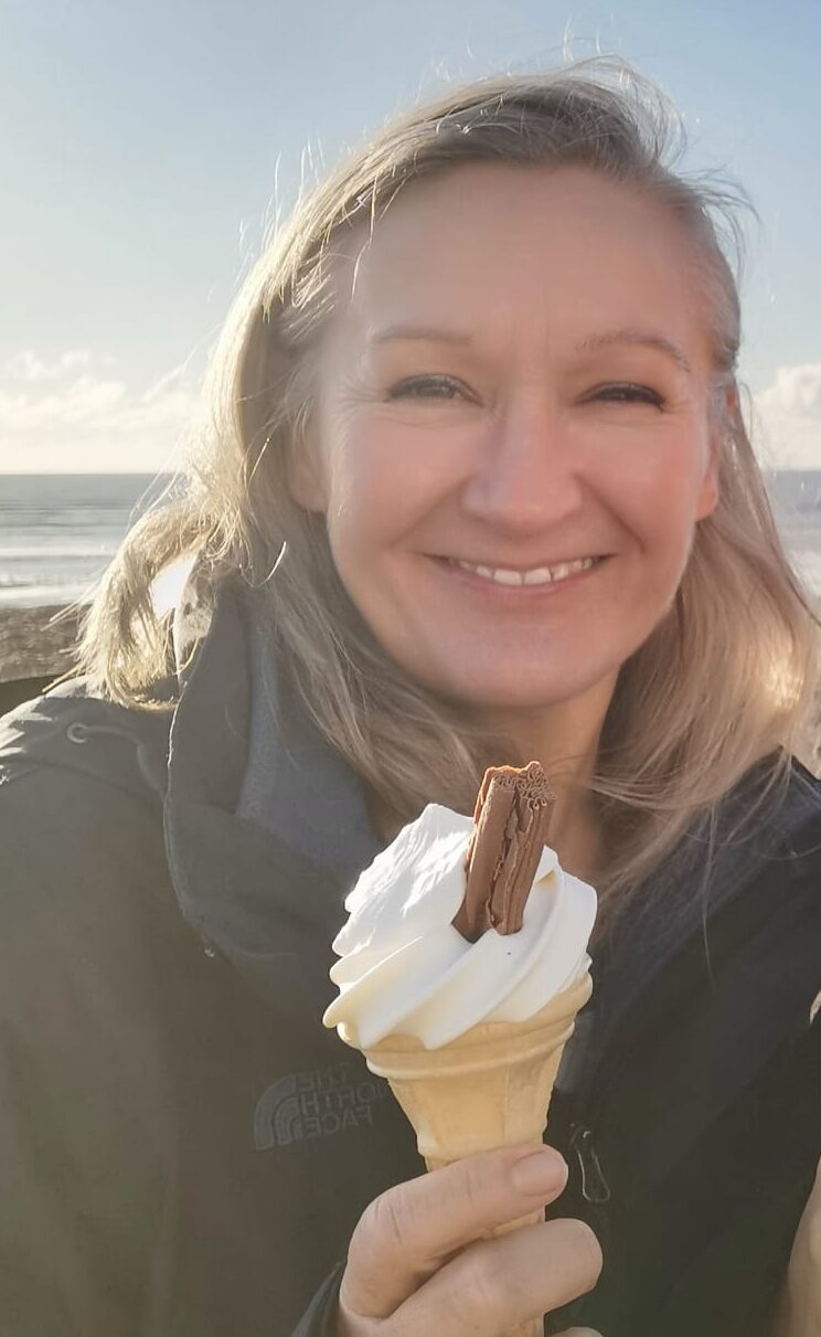 Owner of website holding an ice cream with a big smile. The sea is visible in the background